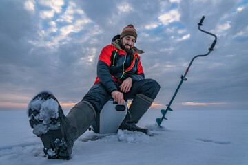 Winter ice fishing. Fisherman on lake catc fish from snowy ice