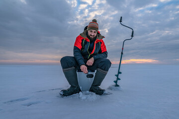 Winter ice fishing. Fisherman on lake catc fish from snowy ice