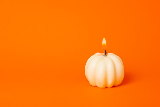 burning miniature white pumpkin candle on orange background with copy space. halloween, thanksgiving, harvest festival concept