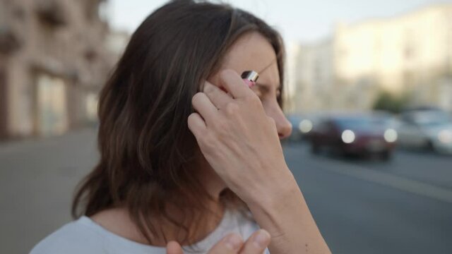 portrait of a brunette on a city street against the background of passing cars is out of focus. the woman thoughtfully smokes a cigarette and removes hair from face. close-up