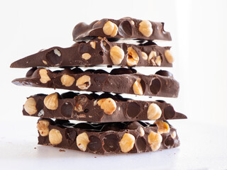 Stack of chocolate. Dark chocolate with whole hazelnuts on white background. Pile of dark chocolate with nuts.