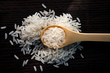 Top view of white rice in wooden spoon on dark wooden table. 