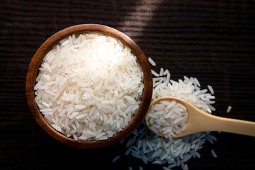 Top view of white rice in wooden bowl on dark wooden table