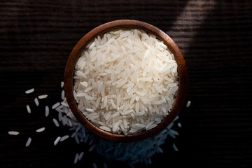 Top view of white rice in wooden bowl on  dark wooden table.