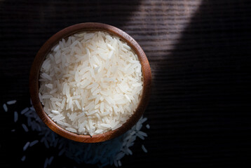 Top view of white rice in wooden bowl on dark wooden table