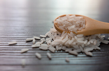 White rice in wooden spoon on dark wooden table. Selective focus.