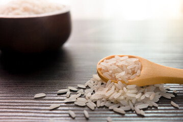 White rice in wooden spoon on dark wooden table. Selective focus.