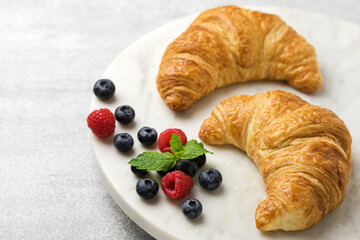 Two fresh croissants on a marble stand with wild berries, light background