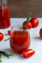 red tomato juice and fresh tomatoes on the white. tomato juice in a glass with green rosemary...
