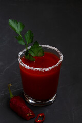 Tomato juice with pepper, spices, salt and ice in glass with copy space. Bloody Mary cocktail. Alcoholic drink with vodka, vampiro cocktail on the black background. vertical.