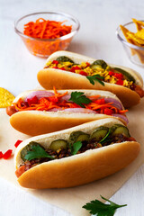 hot dog with vegetables.close-up tasty homemade Hot dogs with different toppings: pickles, fried onion, tomatoes and carrots with green on a white background with copy space.Fast food concept.vertical