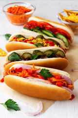 hot dog with mustard.tasty homemade Hot dogs with different toppings: pickles, fried onion, tomatoes and carrots with green on a white background with copy space. Fast food concept. vertical