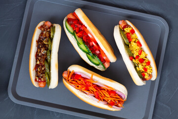 hot dog with mustard and ketchup.tasty Hot dogs with different toppings: pickles, fried onion, tomatoes and carrots with green on a black background with copy space. flat lay. Fast food concept.
