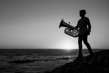 Silhouette of a musician man with a tuba on the sea coast. Black and white photo.