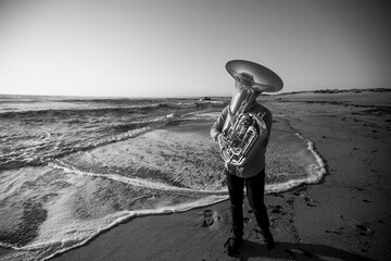 A musician with a tuba on the seashore. Black and white photo.