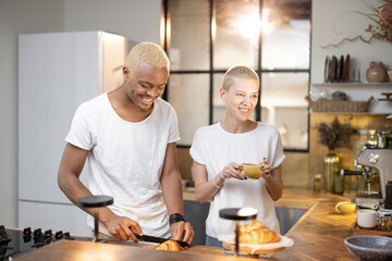 Multiracial couple drinking and toasting drink at home kitchen. Concept of relationship. Idea of modern domestic lifestyle. Black man and european girl spending time together in modern flat