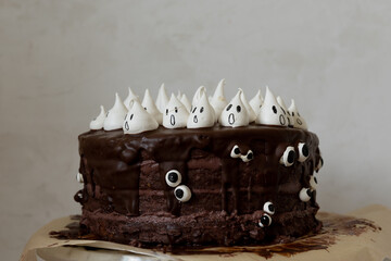 Halloween themed chocolate cake with chocolate cream, chocolate glazing and white meringue ghosts and googly eyes
