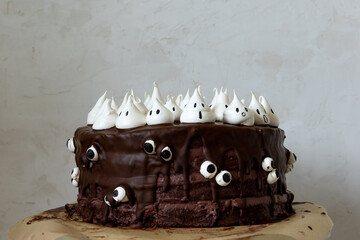 Halloween themed chocolate cake with chocolate cream, chocolate glazing and white meringue ghosts and googly eyes