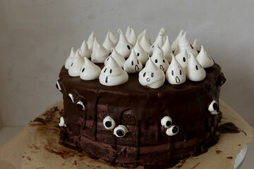 Halloween themed chocolate cake with chocolate cream, chocolate glazing and white meringue ghosts and googly eyes