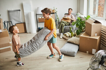 Portrait of two boys building pillow fort in room with boxes while family moving in to new house,...