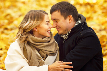 Fototapeta premium Young laughing man and woman hugging in the autumn park. Romantic couple on a date. Love and tenderness in a relationship. Close-up.
