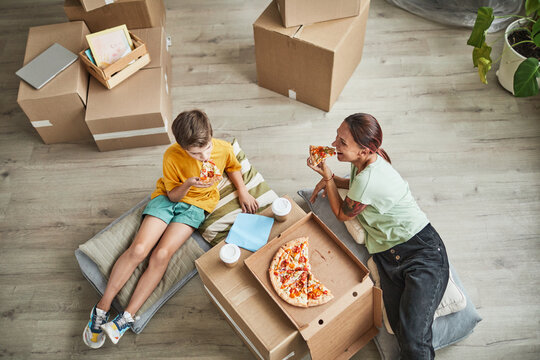 High angle portrait of young mother and son eating pizza from cardboard box while celebrating moving in to new house, copy space