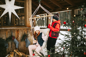 two children boy and teenage girl sitting in swing hammock on porch of village house and having fun during Christmas winter holidays, Christmas and New year vacation concept