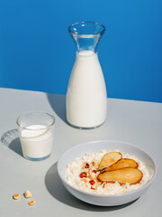 Oatmeal porridge with fresh pear slices, chopped almonds and hazelnuts. Healthy breakfast concept. White wooden table. Closeup view. Bowl on grey textile.