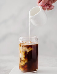Iced coffee in a tall glass with cream poured over. Cold black coffee with ice cubes in a high glass pour cream