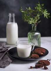 Plate with Chocolate cookies with nuts and glass of milk on dark background. Nordic style.
