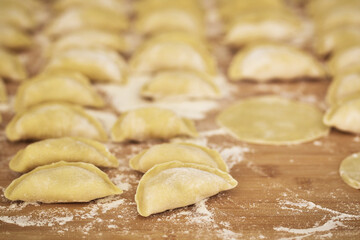 Raw dumplings on a wooden board. The process of making dumplings. Traditional homemade food. Slavic traditional dish. Dough for dumplings. Close up. Top view