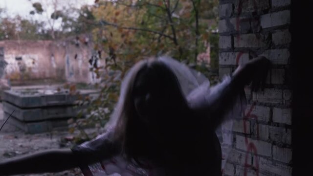 Halloween. A young woman in a wedding dress and veil stands on the roof in the doorway of an abandoned building. Ragged pace of movements. The concept of horror and screamer. 4k