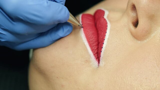 Make-up master prepare woman lips for permanent makeup beauty procedure, holds pen draws dots denotes a line, close up view