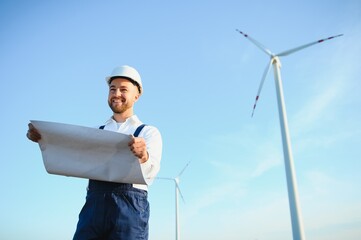 Engineer is checking energy production on wind turbine. Worker in windmills park in helmet.