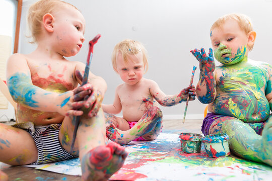 Three messy babies with painted color on their bodies playing with paints