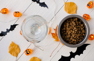 Cat food in the bowl and glass of water on halloween background top view
