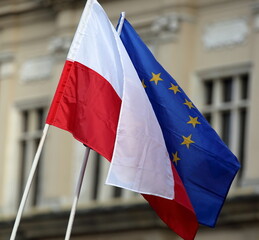 Flags of Poland and European Union on flagpoles, together, outdoor, against building in urban area