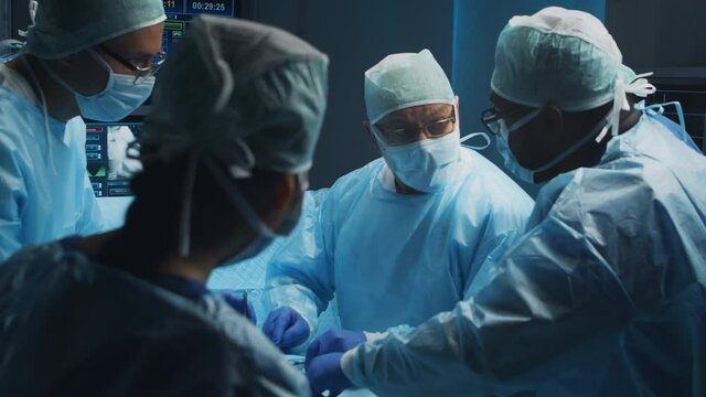 Multiracial team of professional medical surgeons performs the surgical operation in a modern hospital. Doctors are working to save the patient. Medicine, health, cardiology and transplantation.