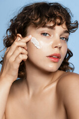 Vertical shot of beautiful girl with curly hair, using face mask on cheek, applying daily care...