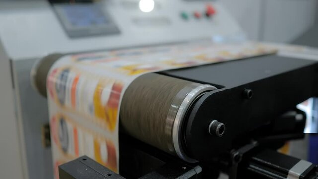 Conveyor of slitter rewinding inspection machine with fast moving printed labels at printer exhibition, trade show - close up. Technology, manufacturing, food packaging, advertising concept