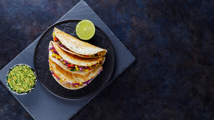 Vegetarian tacos with sweet corn, purple cabbage and tomatoes on a black plate. Tacos with...