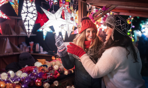 Two friends buying Christmas decoration on winter market booth