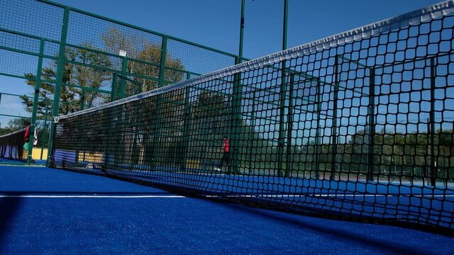 Close-up of a paddle tennis court net and people playing in the background.