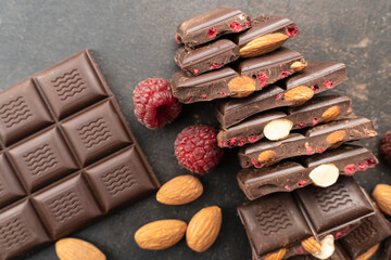 chocolate bars with almonds, raspberries, handmade sweets. Composition of bars and pieces of dark almond chocolate, raspberries on a black background, top view. Pastry craft on the table