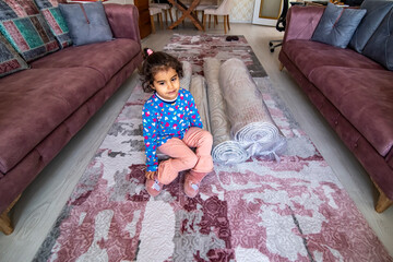 Sweet girl sitting on rolled up carpets after washing in the living room. Carpet cleaning concept