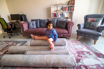 Sweet girl sitting on rolled up carpets after washing in the living room. Carpet cleaning concept