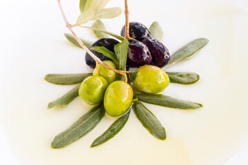 New crop mixed olives and fresh leaves on oil at white surface,harvest concept