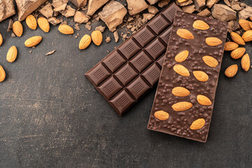 Store Cooking chocolate bars with almonds handmade sweets. Composition of bars and pieces of dark almond chocolate on a black background, top view. Pastry craft on the table