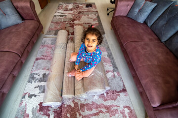 Sweet girl sitting on rolled up carpets after washing in the living room. Carpet cleaning concept