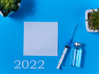 2022, medicine and Vaccination concept. Close up view photo of empty sheet of paper, 2022 goals,syringe, vaccine bottle and two succulents on blue background. Christmas medical card. To do list